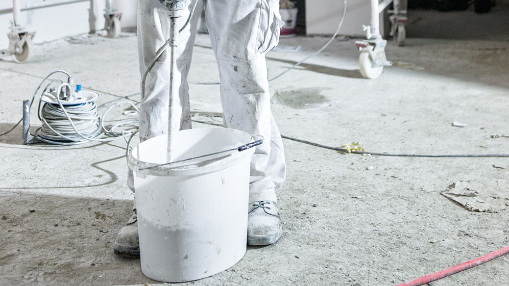 Maler rührt mit elektrischem Rührgerät Putz in einem Eimer