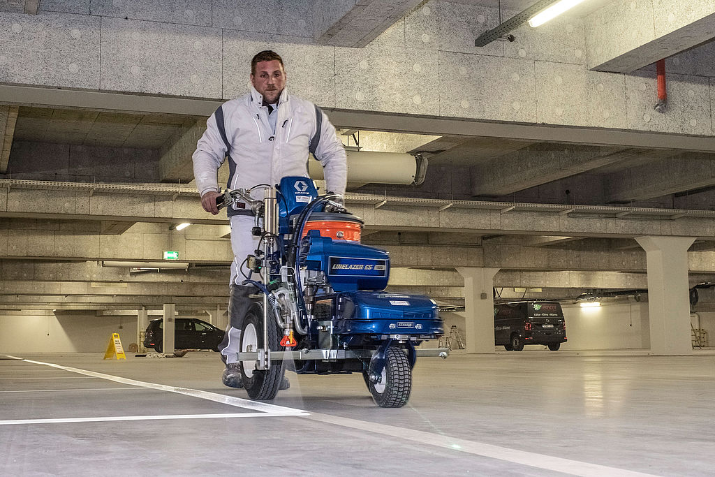 Arbeiter fährt zieht mit einer Bodenmarkierungsmaschine eine weiße Linie in einem Parkhaus